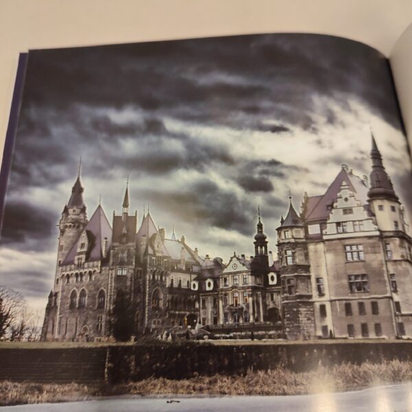 Otwarta książka ze zdjęciem pałacu tle zachmurzonego nieba. w Mosznej na